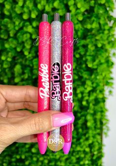 two pink and silver glittered lip glosses in front of a green hedge background