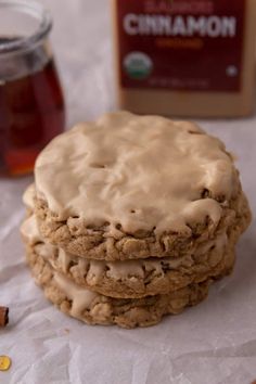 three cookies with icing sitting on top of paper next to a jar of honey