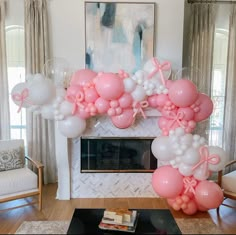 a living room decorated with balloons and pink bows on the fireplace mantel, along with a large balloon arch