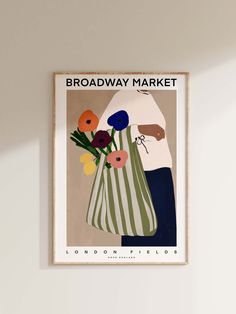 a poster hanging on the wall above a vase with flowers and an image of a woman holding a striped bag