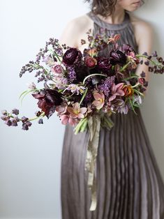 a woman holding a bouquet of flowers in her hand and wearing a dress with pleated skirt