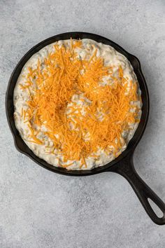 a skillet filled with cheese on top of a gray counter next to a spoon