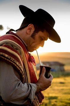 a man in a cowboy hat holding a pipe and looking down at his cell phone