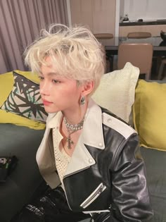 a woman sitting on top of a bed wearing a black jacket and silver necklaces