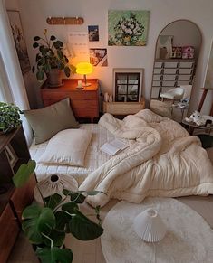 an unmade bed sitting in a bedroom next to a lamp and potted plant