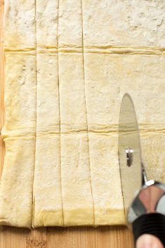 a person cutting bread on top of a wooden table next to a pair of scissors