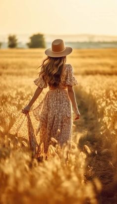 a woman in a dress and hat walking through a wheat field