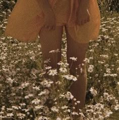 a woman in a yellow dress is standing in a field with daisies and wildflowers