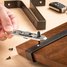 a person is holding a piece of metal on a wooden table next to other tools