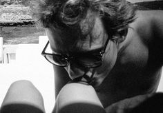 black and white photograph of a man with glasses looking at his cell phone while sitting on the floor