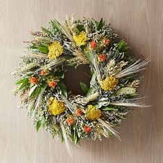 a wreath with yellow flowers and green leaves on a wooden surface in front of a wall