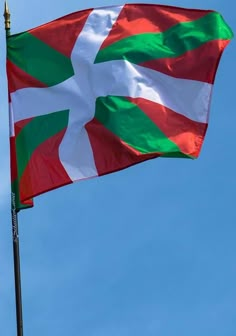 a flag flying in the wind on a pole with a blue sky behind it,