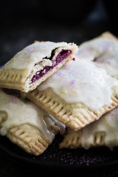 several pastries are on a black plate with white icing and purple sprinkles