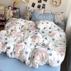 an unmade bed with blue sheets and pink bows on it, in a bedroom