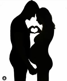 the silhouette of a pregnant couple making a heart shape