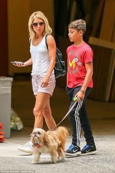 a woman walking a small dog on a leash next to a man in red shirt and white shorts