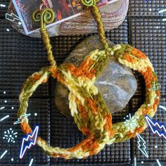 a crocheted bracelet is sitting on top of a rock next to a book