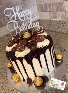 a birthday cake decorated with chocolates and white frosting on a countertop next to a sign that says happy birthday