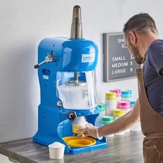 a man standing in front of a blue and white coffee maker on top of a wooden table