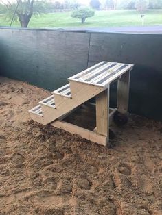 a wooden bench sitting in the sand next to a wall and grass field behind it