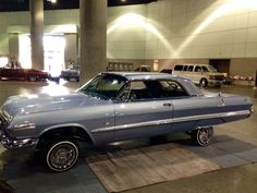 an old blue car is parked in a showroom with other cars and people looking at it