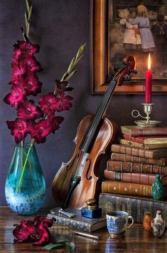 a violin, flowers and books on a table with a candle in the corner next to it