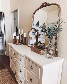 a white dresser topped with lots of drawers next to a mirror and vase filled with flowers