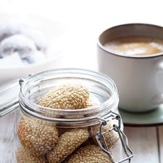 a jar filled with cookies sitting on top of a table next to a cup of coffee