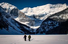 two people walking in the snow near mountains