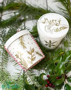 two white christmas boxes sitting on top of evergreen leaves and pine cones with the words merry christmas written on them