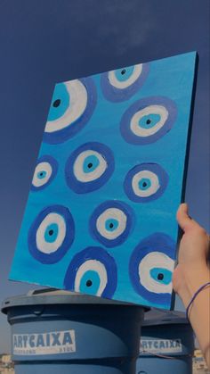 a hand holding up a piece of art that looks like an eyeball pattern on a blue background