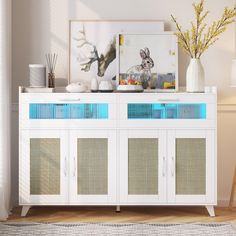 a white sideboard with blue glass doors in a living room next to a painting on the wall