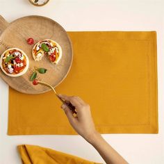 a person holding a spoon over a wooden plate with small pizzas on top of it