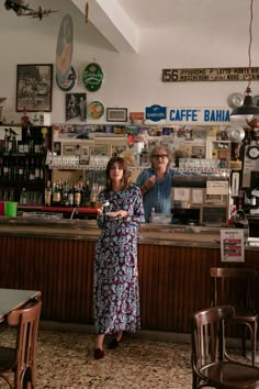 two people standing in front of a counter at a coffee shop with signs on the wall