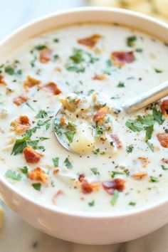 a bowl of soup with bacon, cheese and parsley on the spoon in it