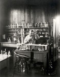 an old black and white photo of a man working in a lab with lots of glassware