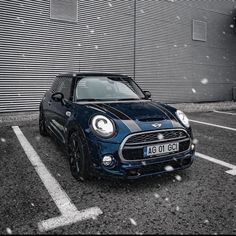 a small blue car parked in front of a building with snow falling on the ground