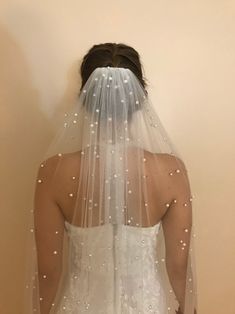 the back of a bride's wedding dress with pearls on it and her veil