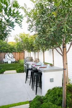 an outdoor dining area with bar stools and table surrounded by greenery in the back yard