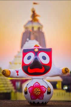 a colorfully painted doll sitting in front of a tall building