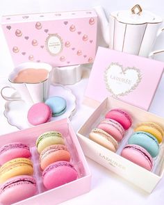 three pink boxes filled with macaroons next to a cup of coffee and tea