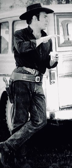 black and white photograph of a man in cowboy attire leaning against a car with the door open