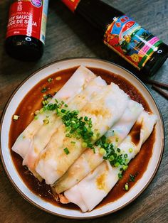 a white plate topped with dumplings covered in sauce and garnished with green onions