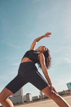 a woman in black shirt and shorts doing yoga pose on the street with buildings in the background