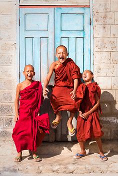 three young monks laughing and jumping in front of a blue door with white shutters