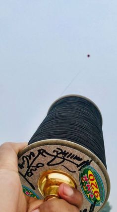 a hand holding a spool of thread with a kite in the sky behind it