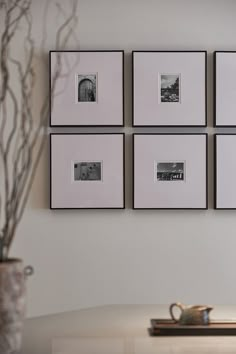 four framed photographs hang on the wall above a table with a vase and coffee cup