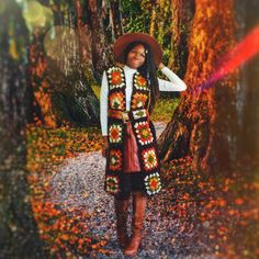 a woman standing in the woods wearing a crocheted vest and hat with sunflowers on it