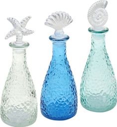 three different colored glass vases with sea shells on top, one blue and one green