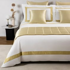 a white and yellow bed with pillows on top of it in a living room next to a night stand